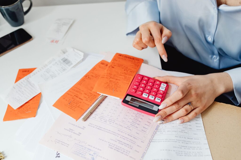 Hands working a calculator over receipts and invoices on a desk, the math behind CAC, ROAS and payback period