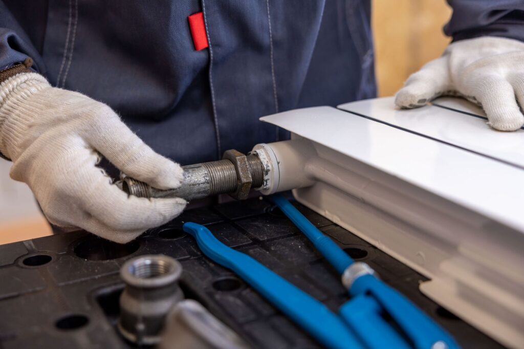 Plumber in work gloves fitting a threaded pipe to a radiator, a booked job of the kind a Google Ads budget has to pay for