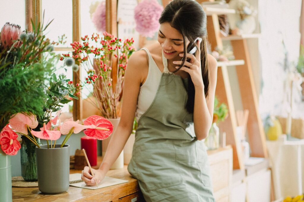 Florist taking a customer's phone call and writing down the order in her shop, the kind of call a Google Business Profile brings a local business