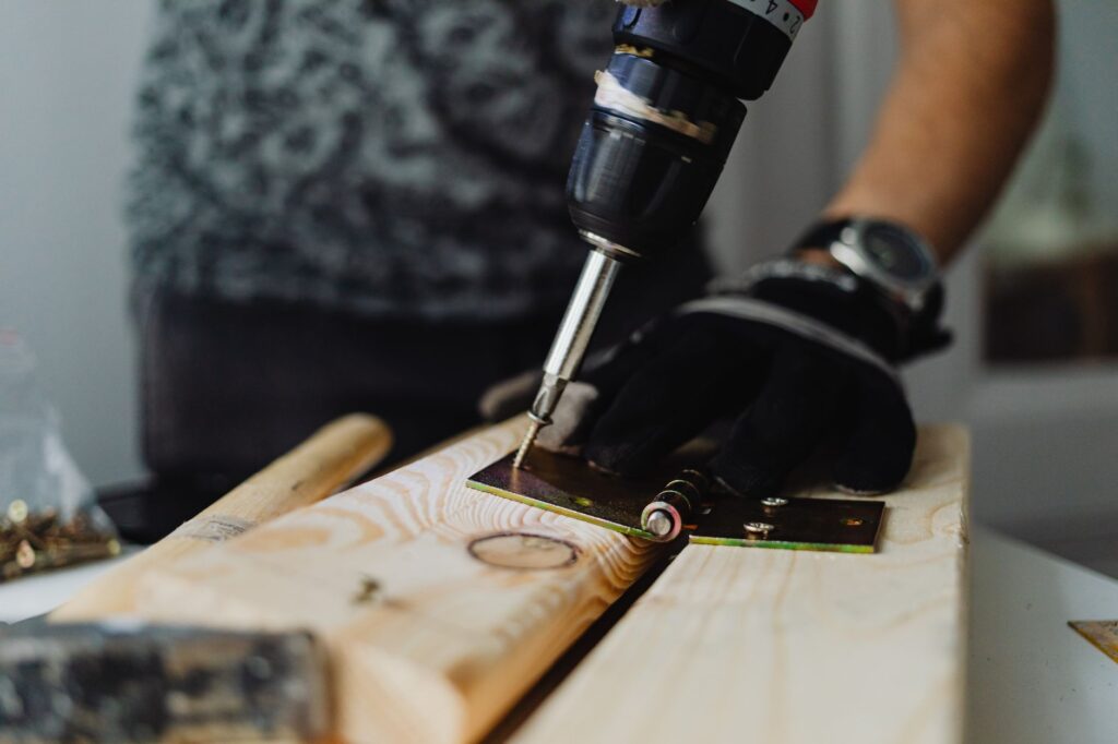 Gloved hands driving a screw into a door hinge on a wooden board, the kind of local service job a small Google Ads budget has to pay for